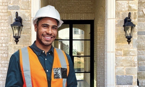 Man in construction hat standing in front of house with iron door