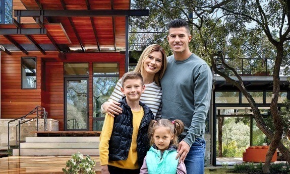 Family of four smiling in front of home with custom iron doors and windows